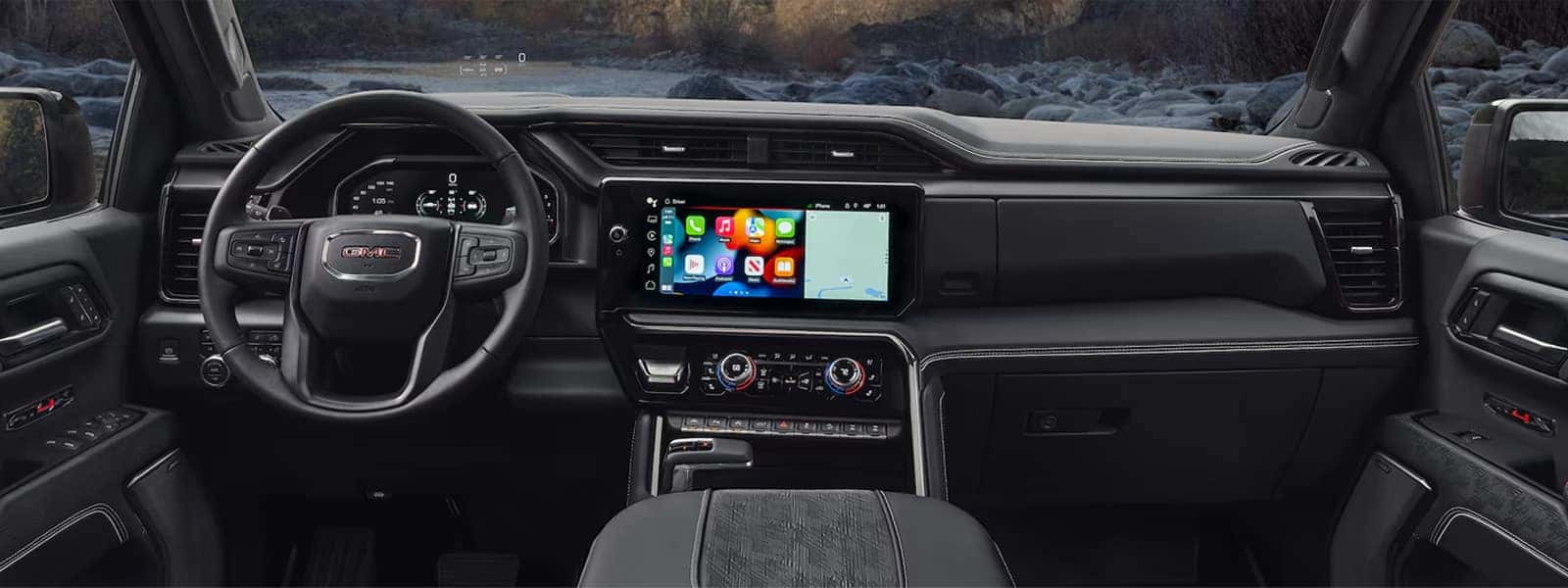 Front interior view of the 2026 GMC Sierra 1500 showing the steering wheel, digital instrument cluster, wide center touchscreen, and driver-focused dashboard layout.