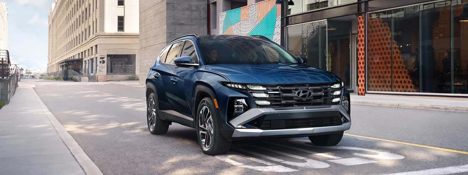 Blue Hyundai Tucson Hybrid SUV parked on a modern city street, showcasing the bold front grille and LED lighting design.