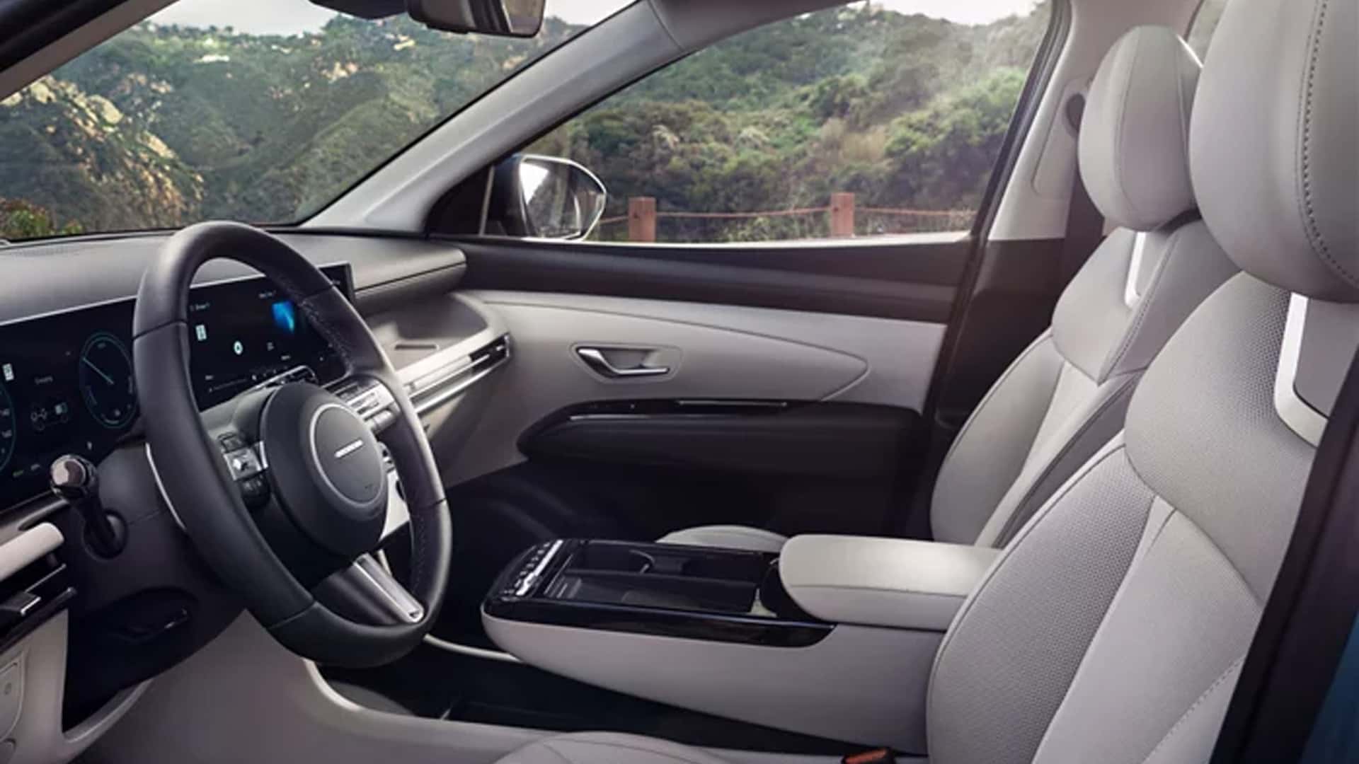 Driver and front passenger area of the Hyundai Tucson Hybrid with digital displays, steering wheel controls, and spacious cabin layout.