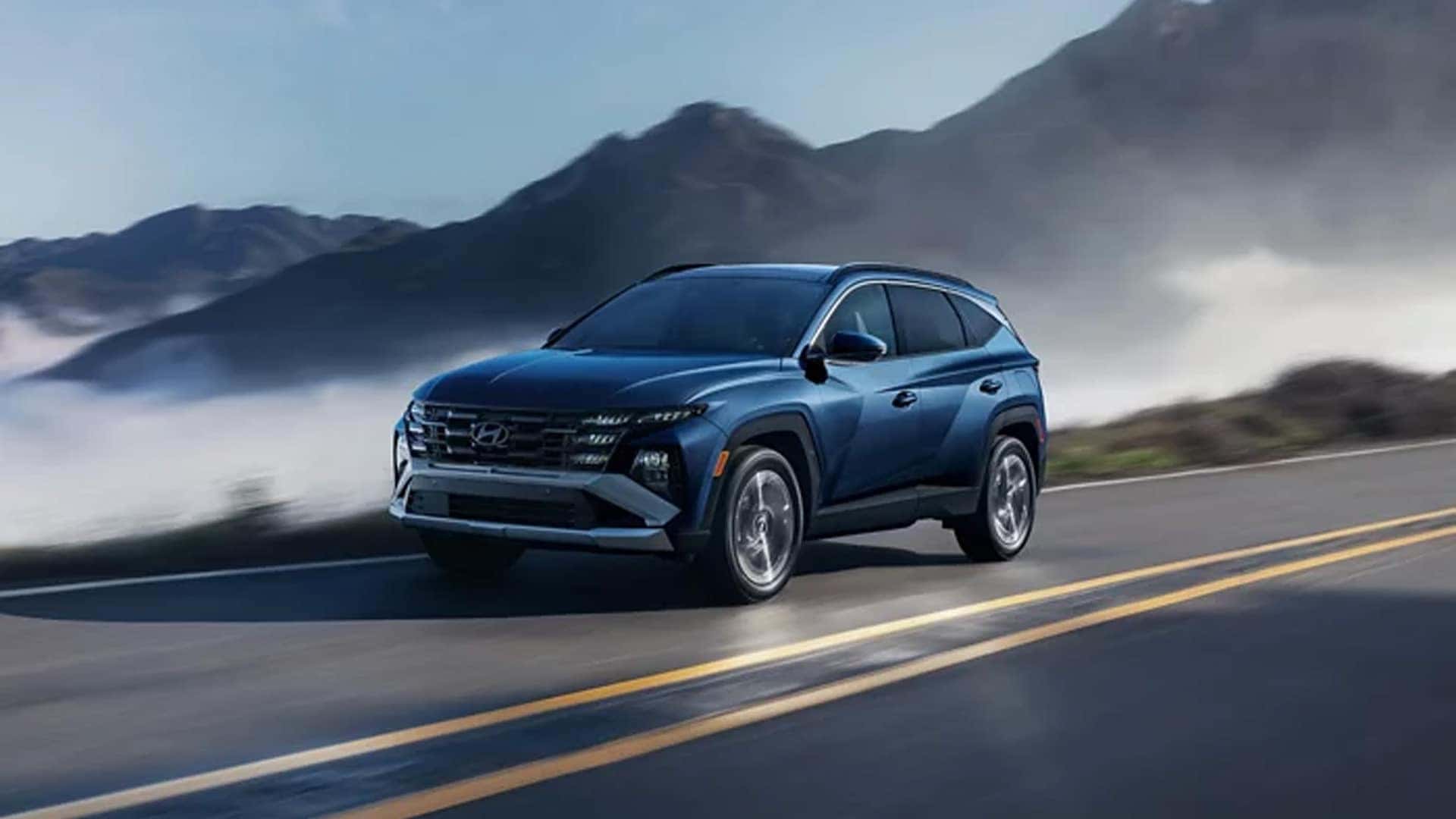 Blue Hyundai Tucson Hybrid driving on a scenic mountain road, highlighting aerodynamic exterior styling and hybrid performance.