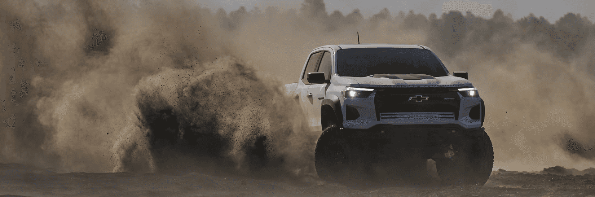 White Chevy Colorado driving off road while kicking up dirt and dust
