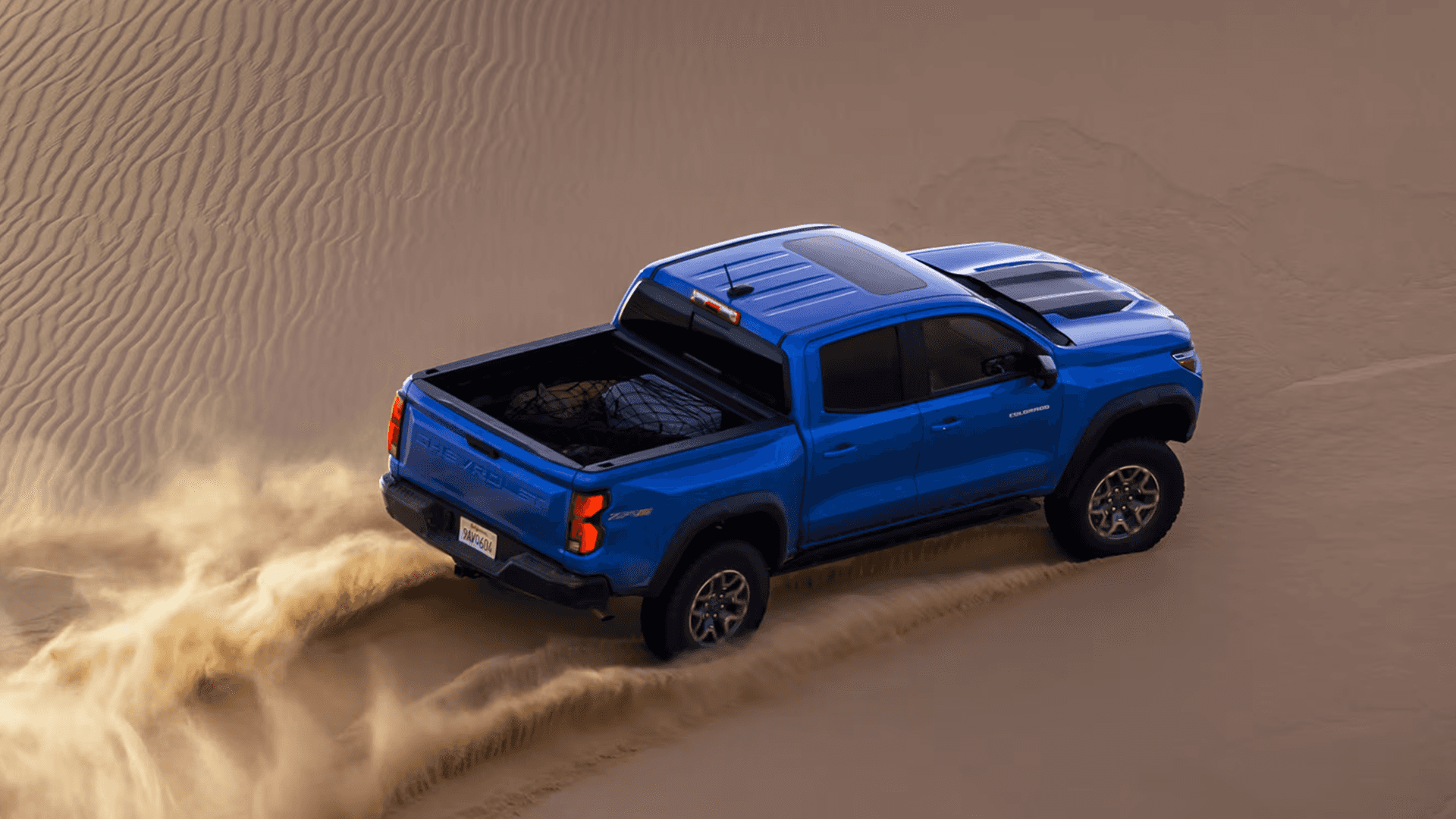 Blue Chevy Colorado driving across sand dunes kicking up dust