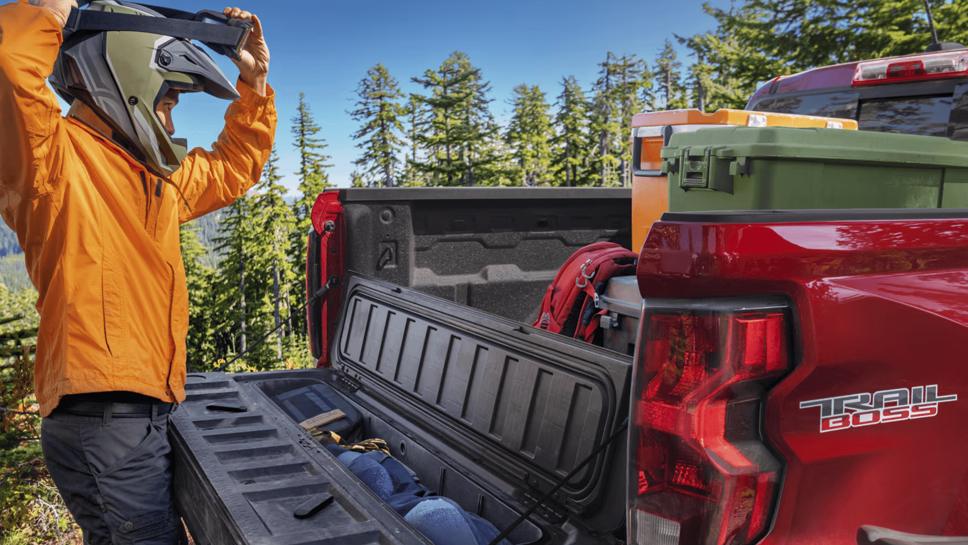 Person loading gear into the Chevy Colorado Trail Boss truck bed with tailgate storage compartment open
