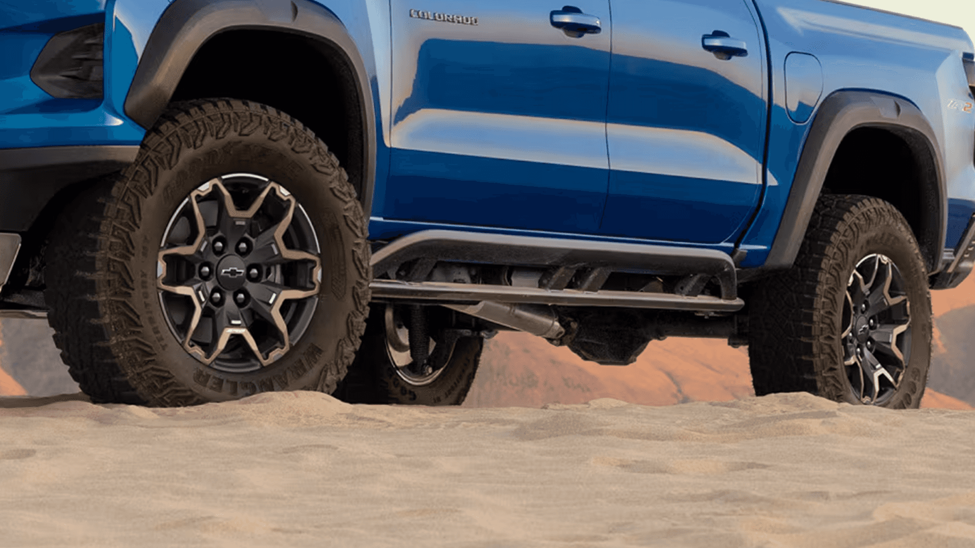 Close up of blue Chevy Colorado wheels and suspension driving on sand