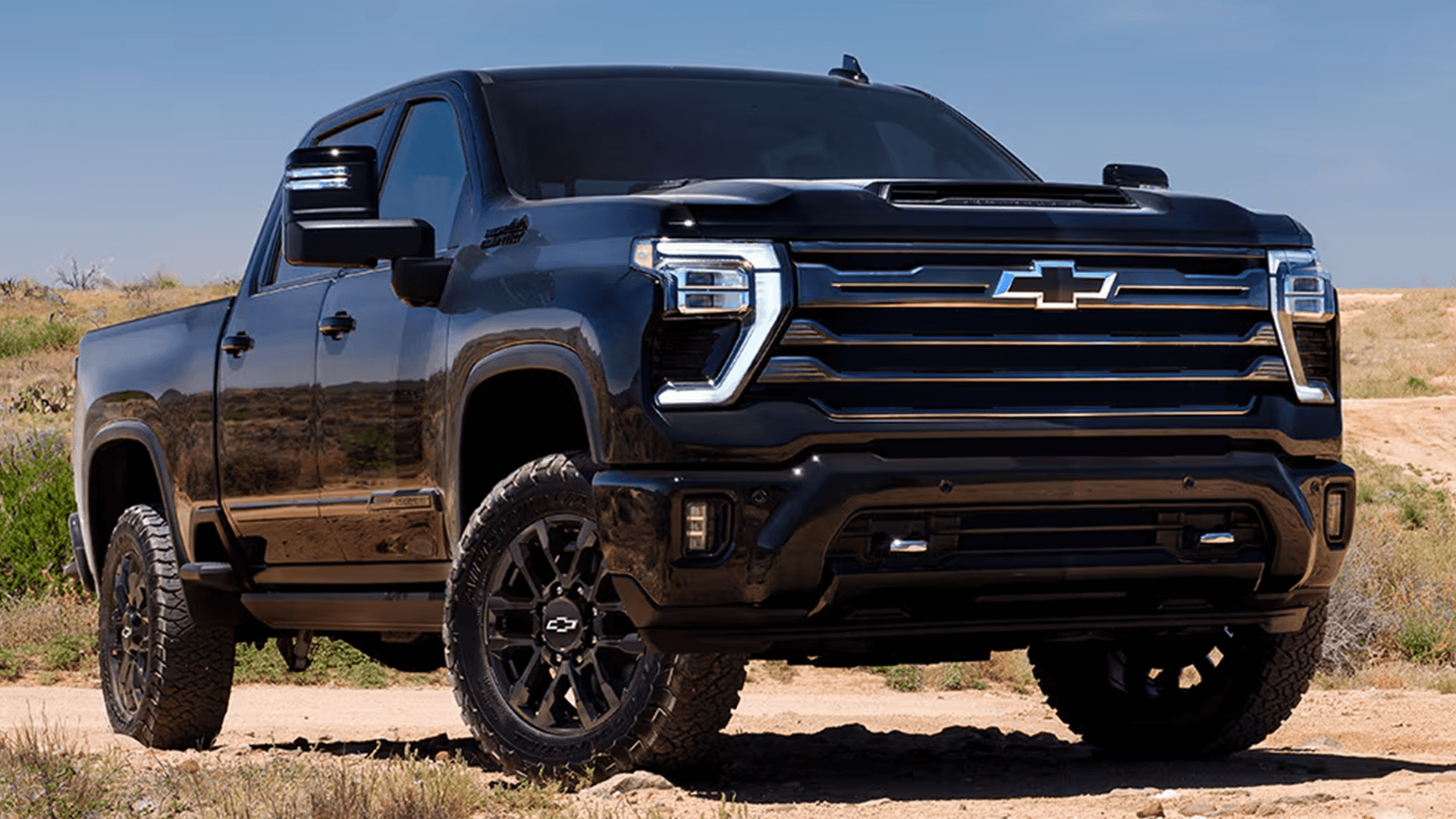 Front three quarter view of black 2026 Chevy Silverado HD with LED signature headlamps and off road tires on a dirt trail