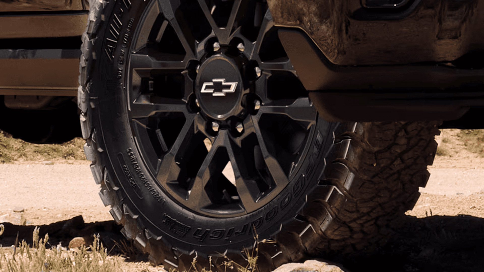 Close up of black Chevy bowtie wheel and all terrain tire on 2026 Silverado HD, showing aggressive tread for off road traction