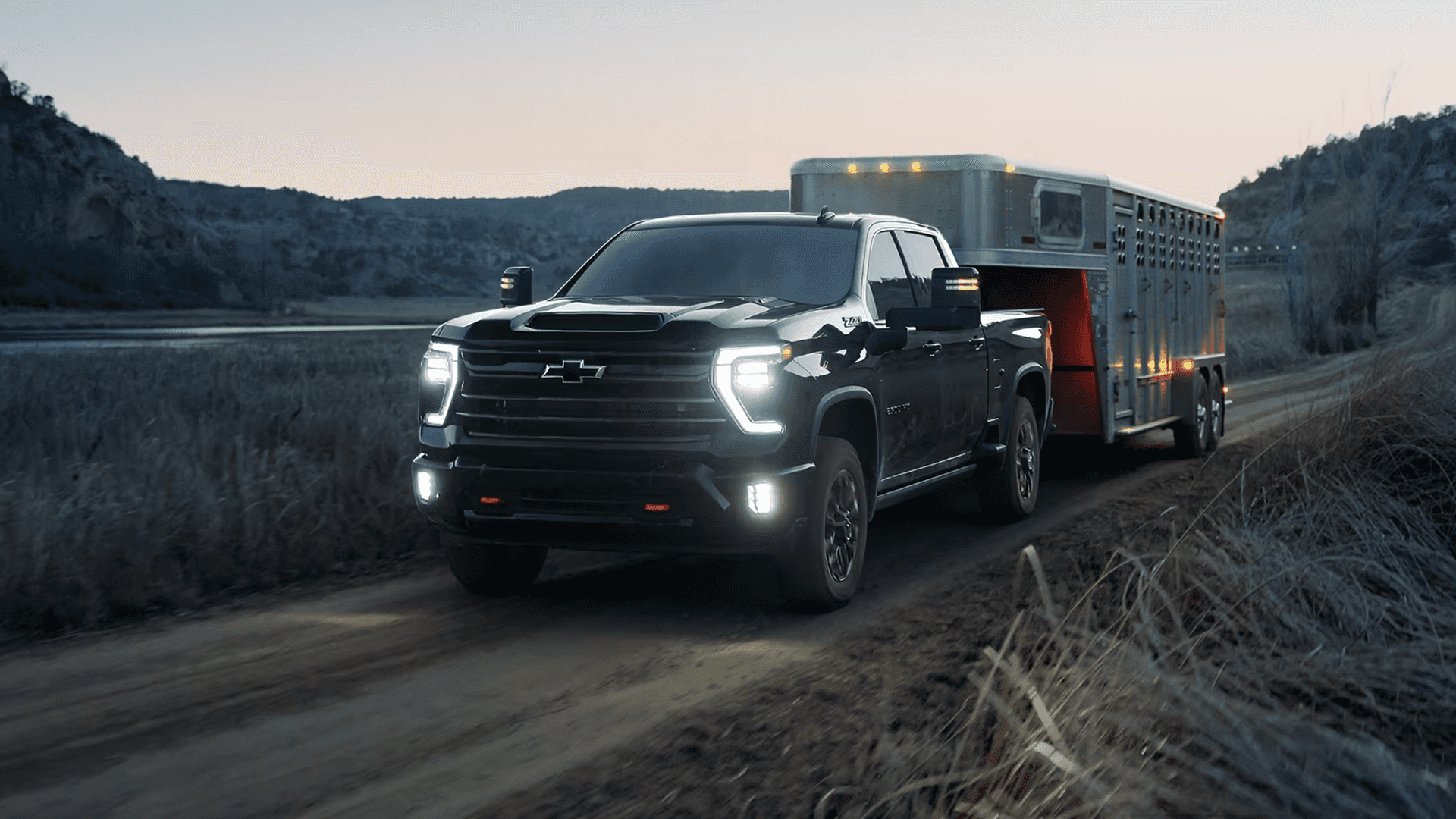 2026 Chevy Silverado HD towing a large trailer on a rural road at dusk