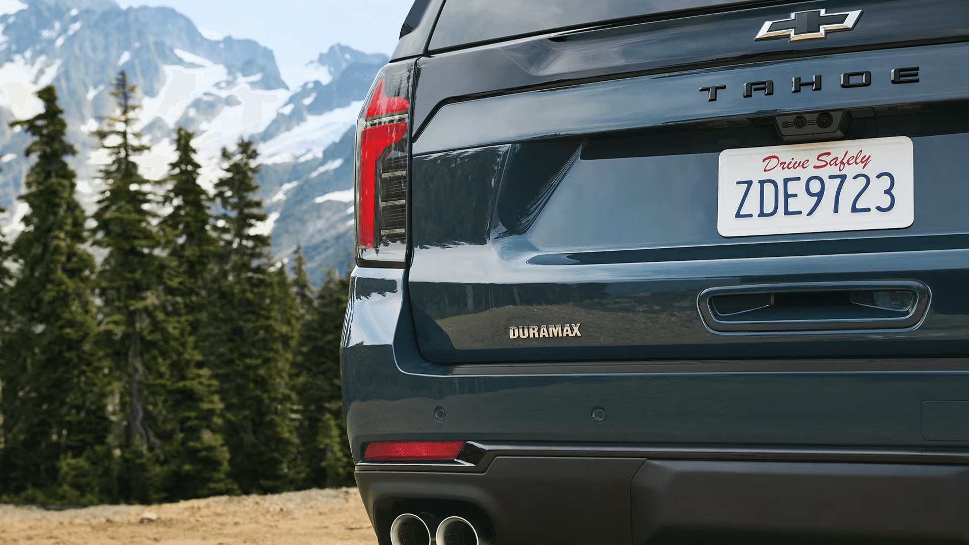 rear three quarter view of a dark blue 2026 Chevrolet Tahoe showing the liftgate, Tahoe badge, and Duramax emblem with mountain background