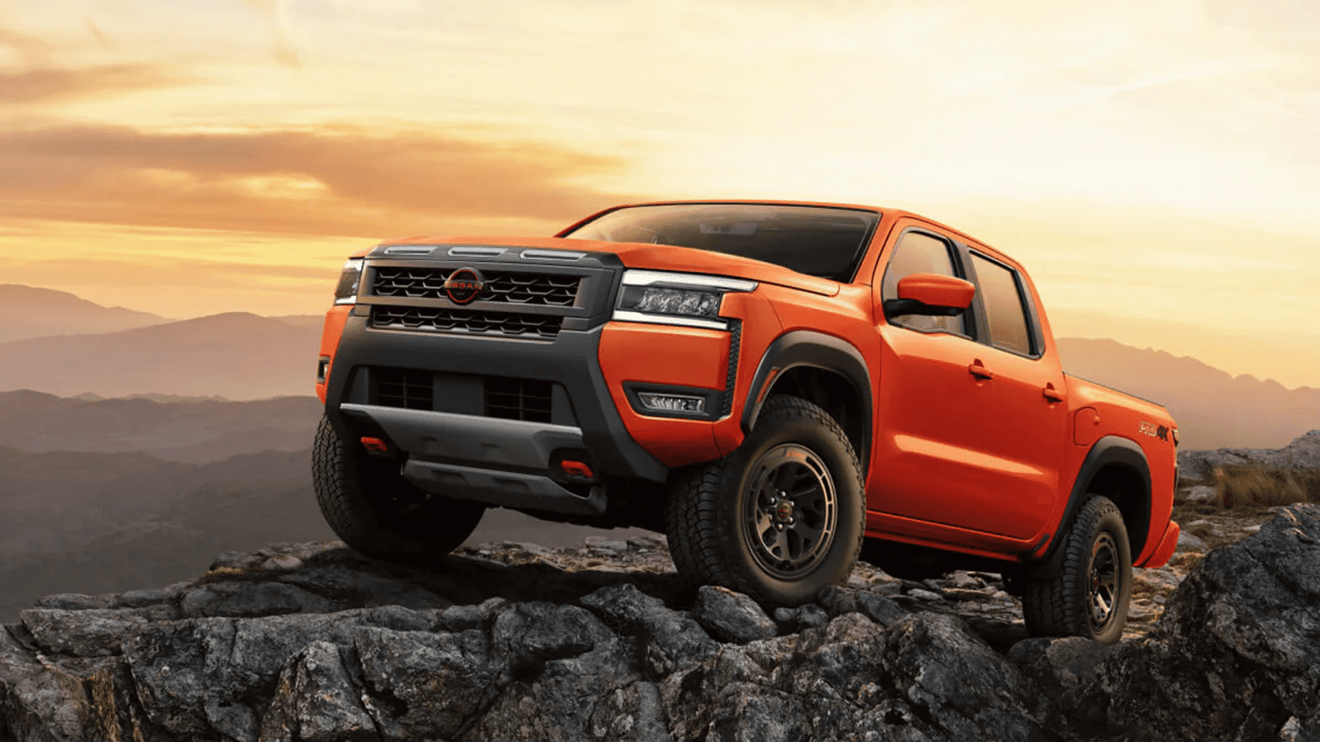 Orange 2026 Nissan Frontier pickup parked on rocky overlook at sunset showing bold grille and off road stance