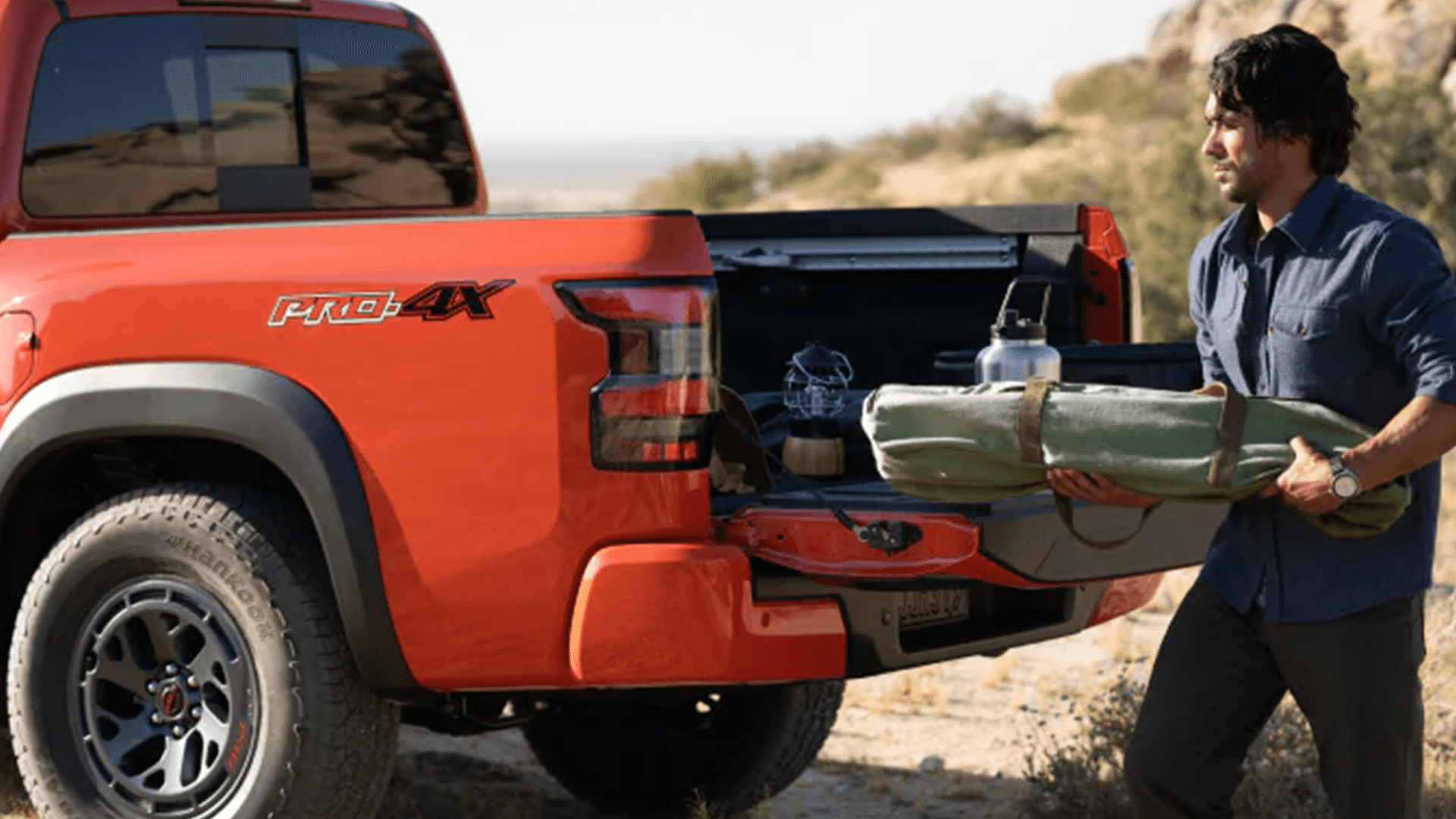 Person loading camping gear into an orange Nissan Frontier truck bed with the tailgate down