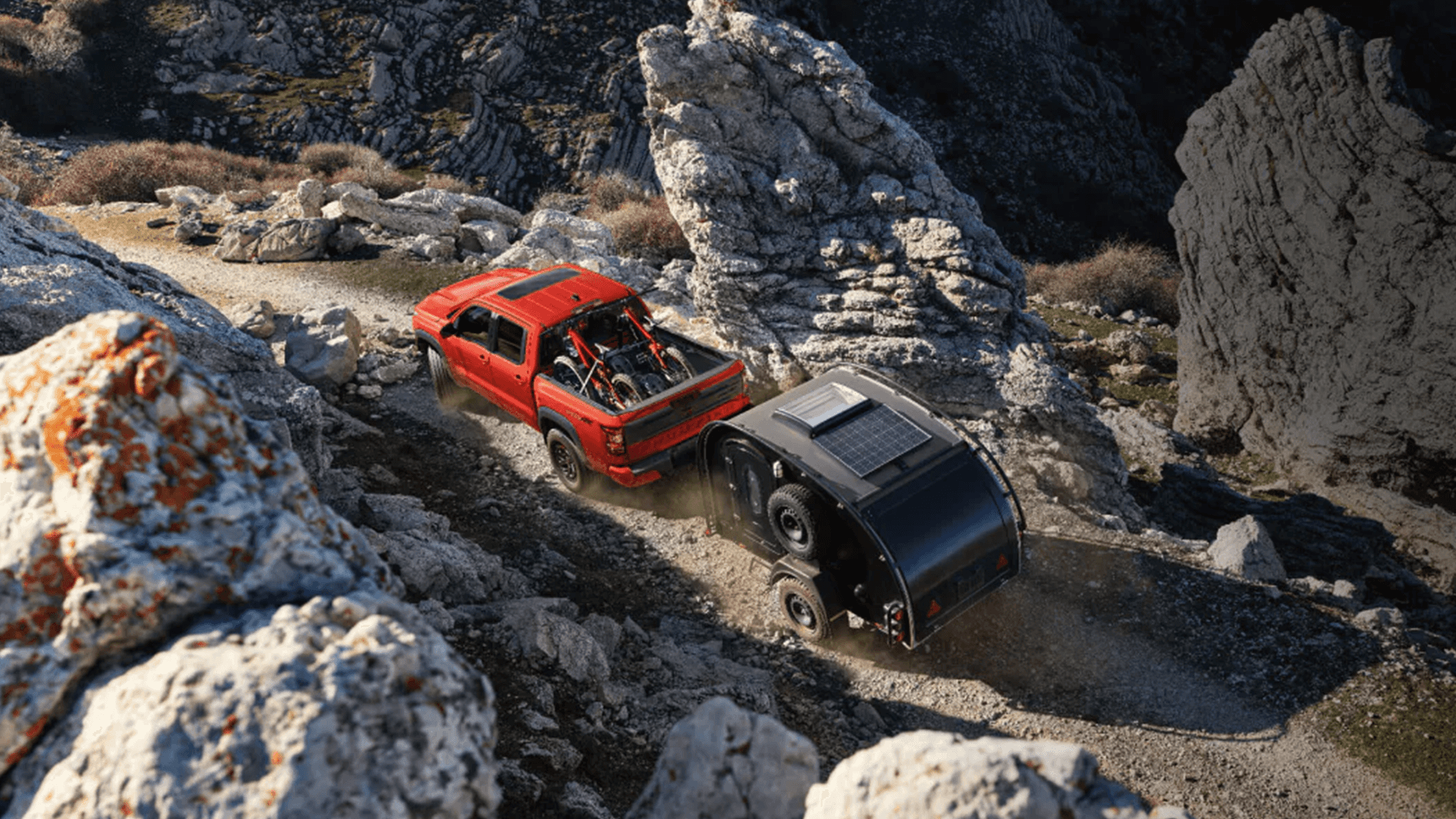 Red Nissan Frontier towing an off road camper on a rocky mountain trail with bikes in the truck bed