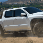 White Nissan Frontier pulling a skid steer on a utility trailer at a construction site