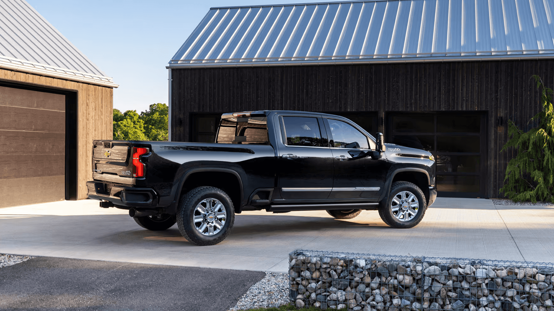 Side profile of a black Chevy Silverado 2500 HD crew cab parked outside a modern barn style building with metal roofs