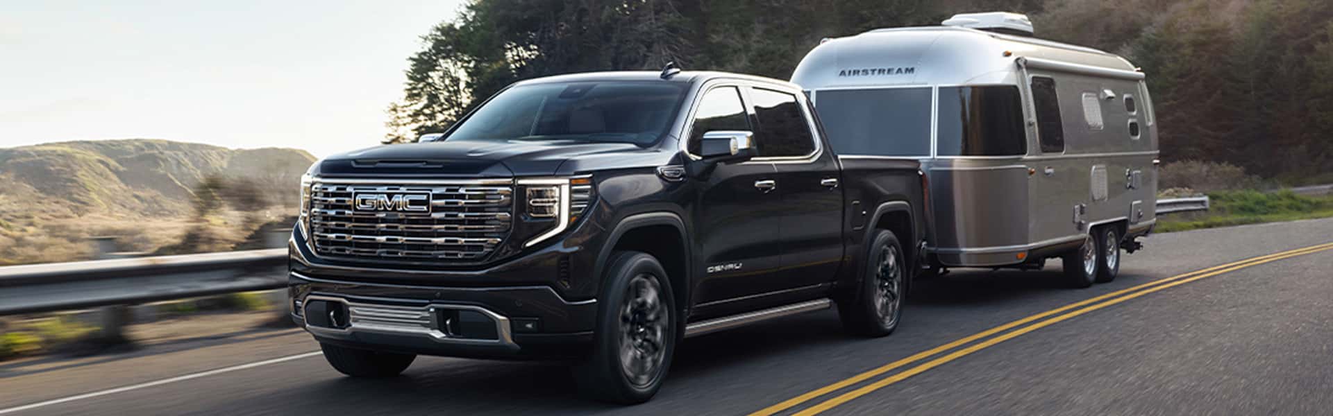 GMC Sierra 1500 pickup truck hauling a silver travel trailer on an open road