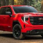Red 2026 GMC Sierra 1500 pickup truck shown in a forest setting highlighting exterior trim design
