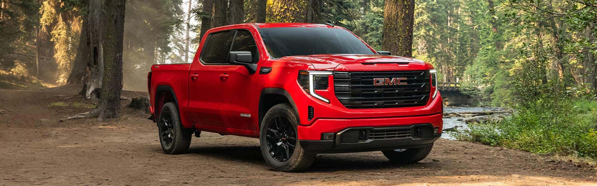 Red 2026 GMC Sierra 1500 pickup truck shown in a forest setting highlighting exterior trim design