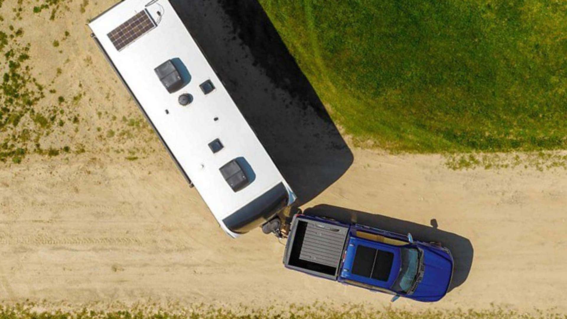 Overhead view of a 2026 Ford F-150 towing a travel trailer on a dirt road, showing turning clearance.