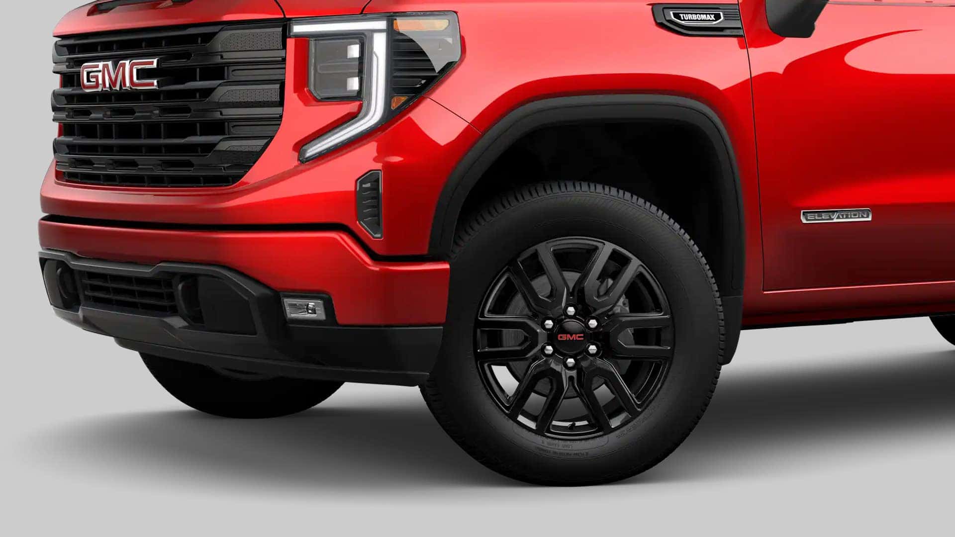 Red 2026 GMC Sierra 1500 Elevation showing black alloy wheels, all-season tires, and aggressive front-end styling.