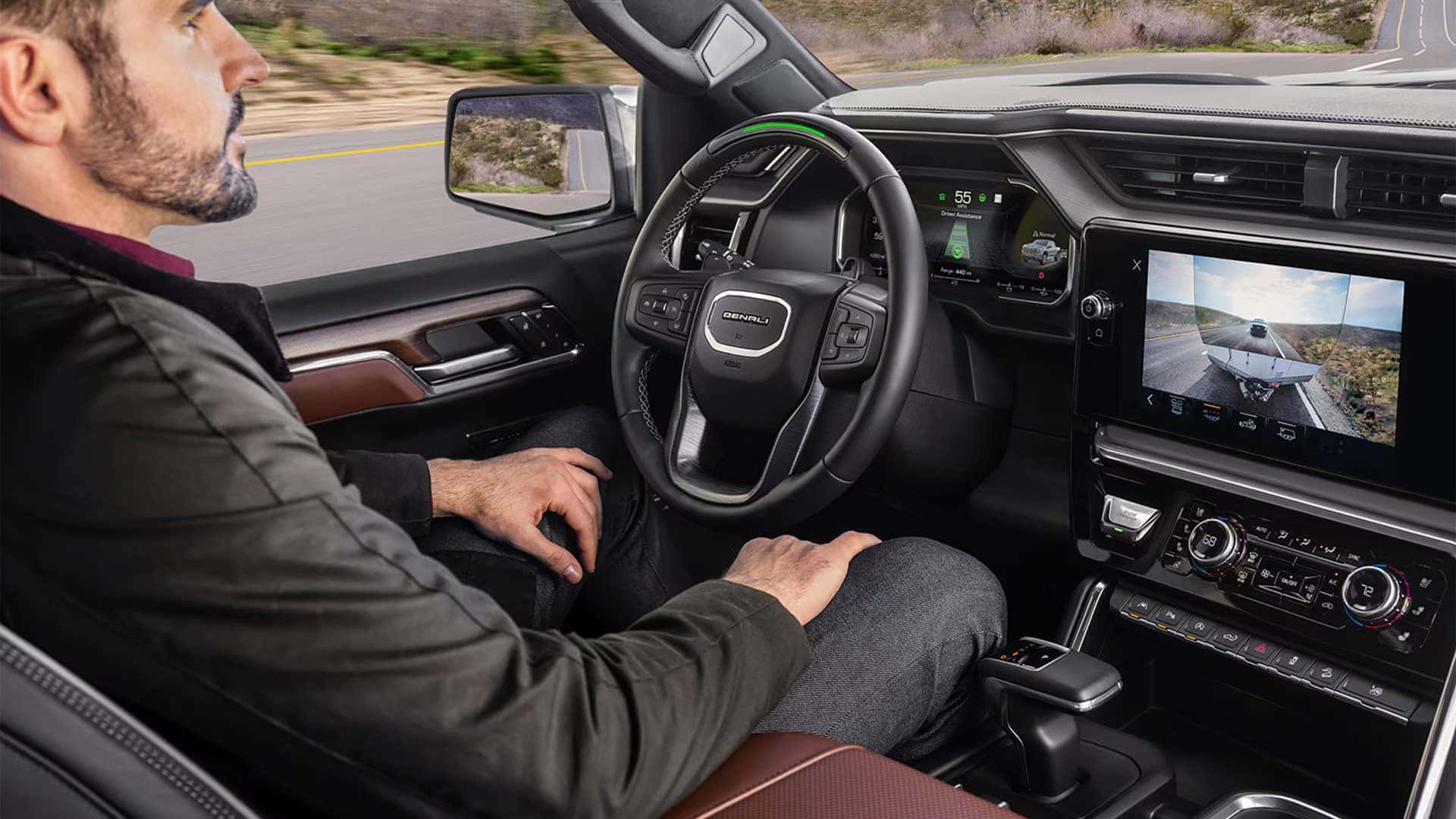 Driver inside a GMC Sierra 1500 viewing a trailer camera feed on the center touchscreen for towing visibility and backing support.
