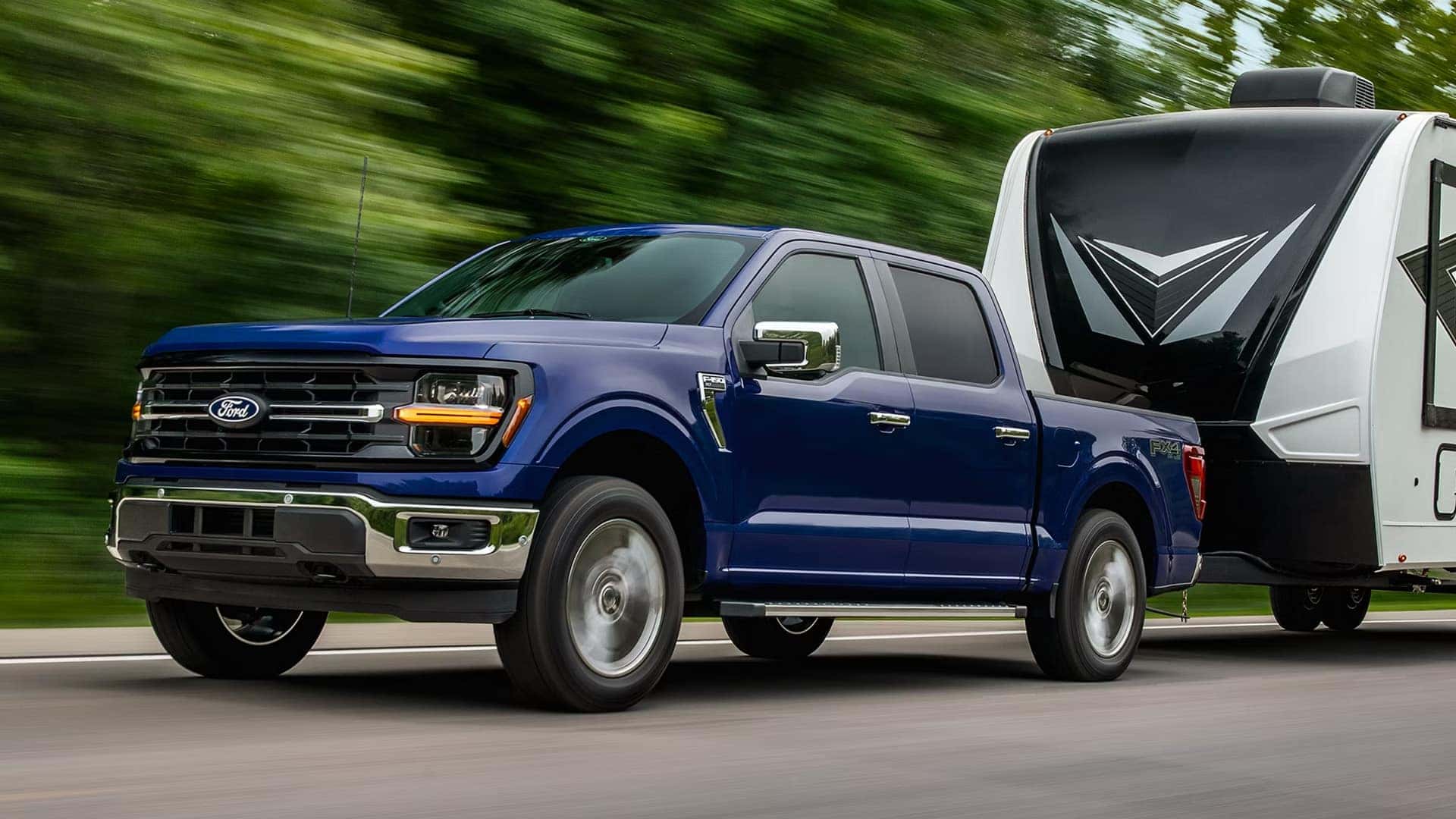 Blue 2026 Ford F-150 towing a travel trailer on the highway, demonstrating trailering capability and on road stability.