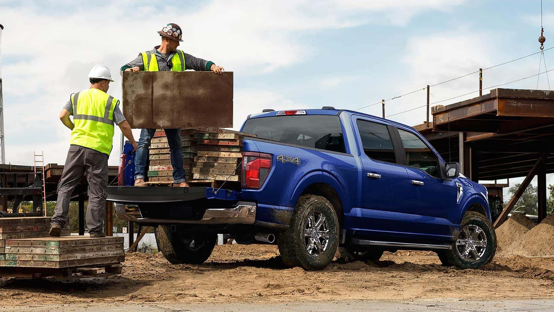 Blue 2026 Ford F-150 hauling construction materials in the bed at a job site with workers loading cargo.