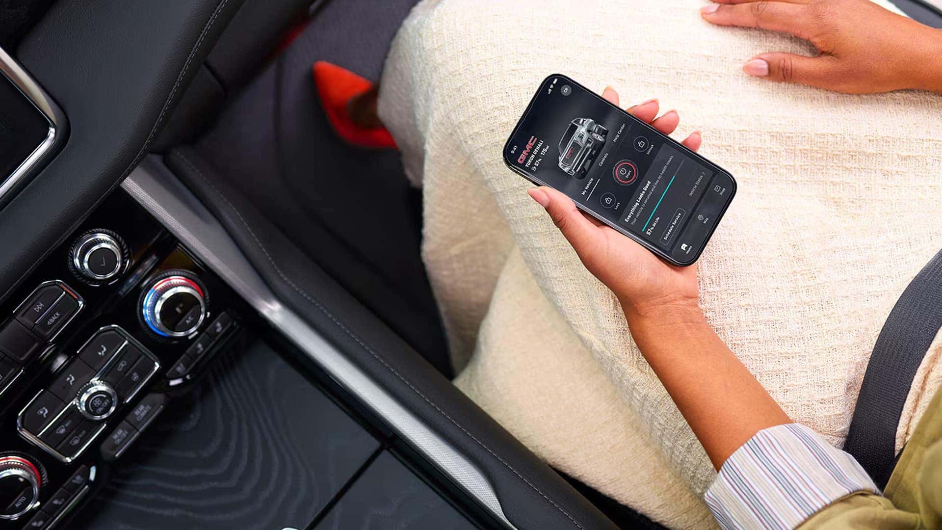 Passenger holding a smartphone with the GMC mobile app open, showing vehicle status and remote features inside the Sierra 1500 cabin.