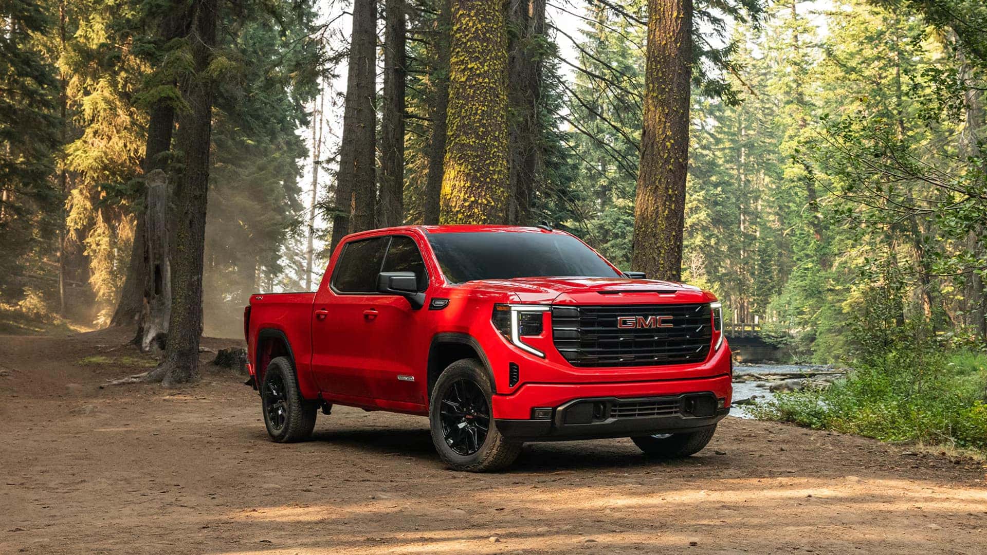 Red 2026 GMC Sierra 1500 parked in a forest setting, highlighting exterior color options and available trim levels.