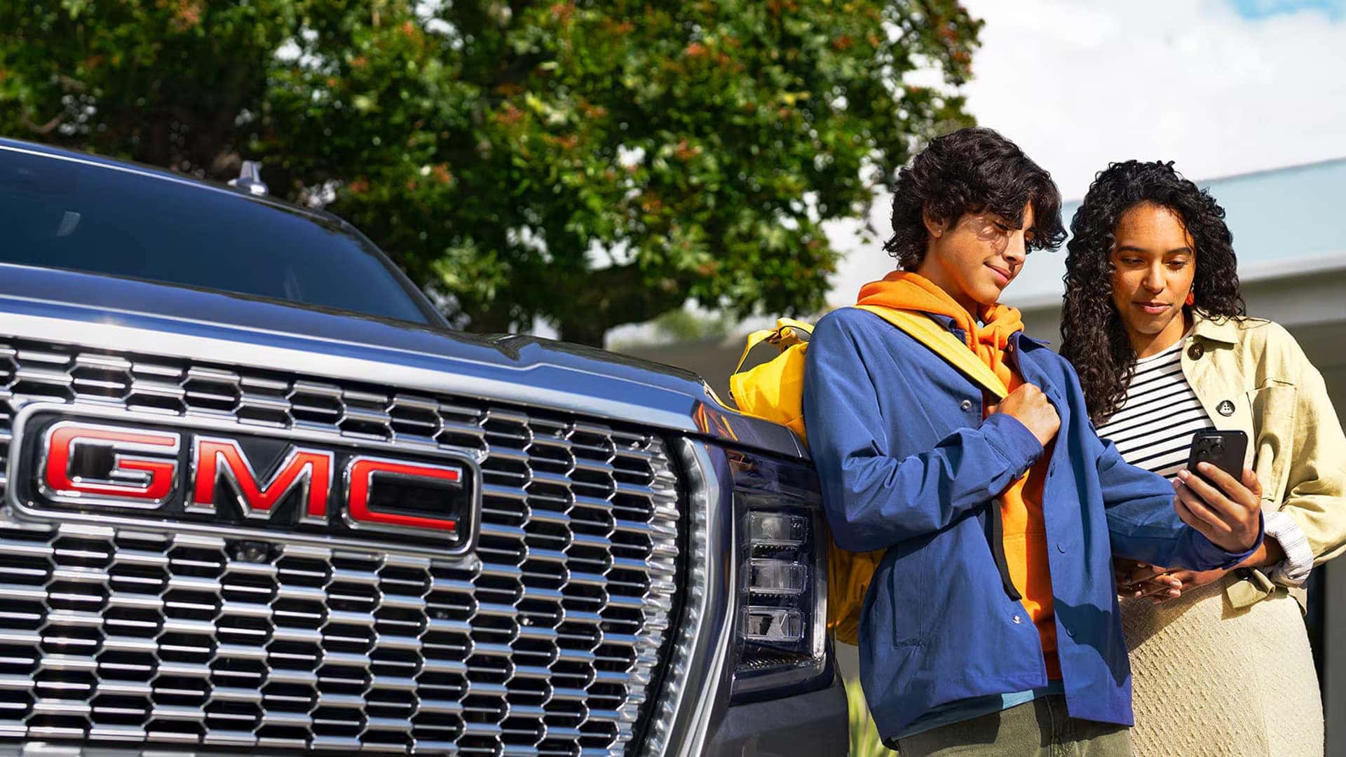 Two people standing near a GMC Sierra 1500 using a smartphone, representing connected vehicle technology and mobile app access.