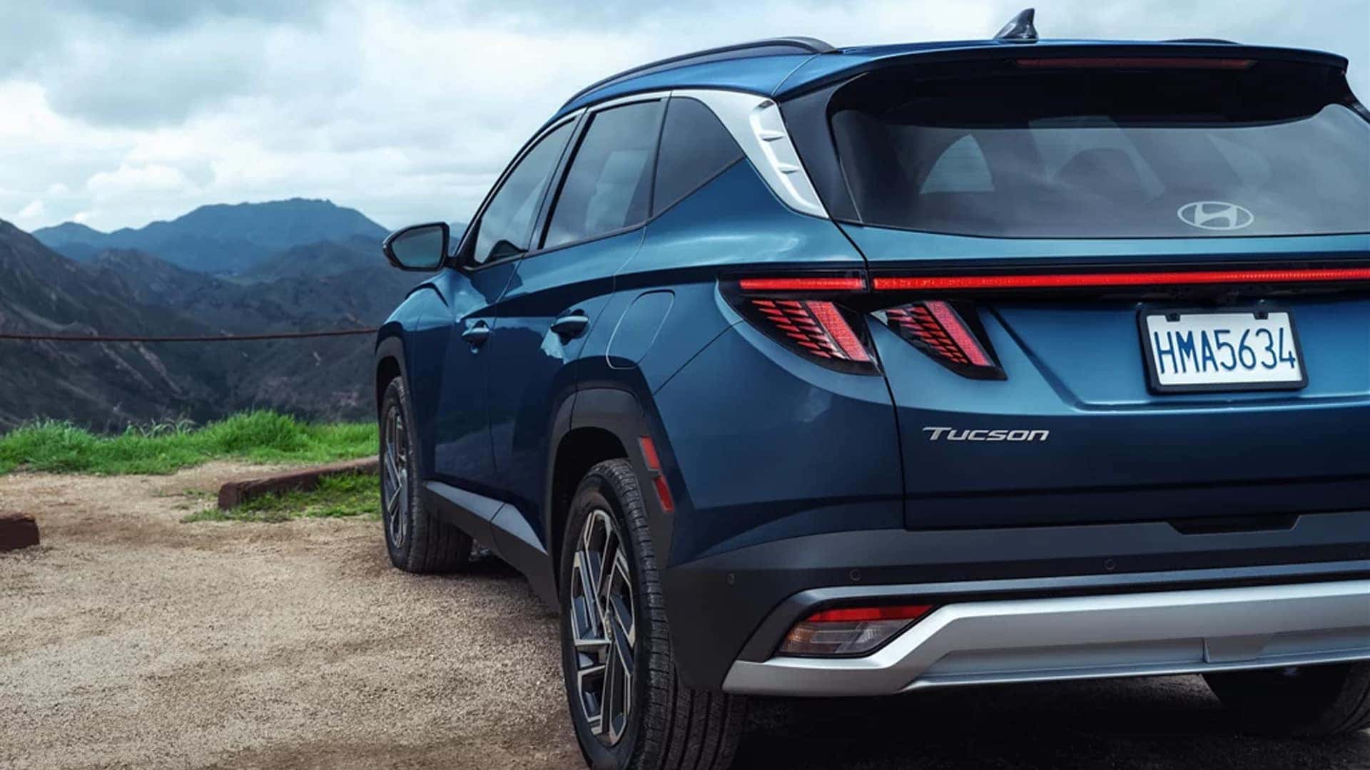 Rear three-quarter view of a blue Hyundai Tucson Hybrid parked near a scenic overlook, highlighting rear design, taillights, and SUV proportions.