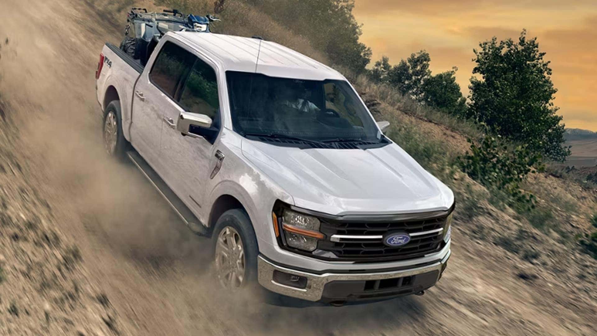 White 2026 Ford F-150 driving on a dirt trail with dust behind it, showcasing off-road capability and 4x4 performance.