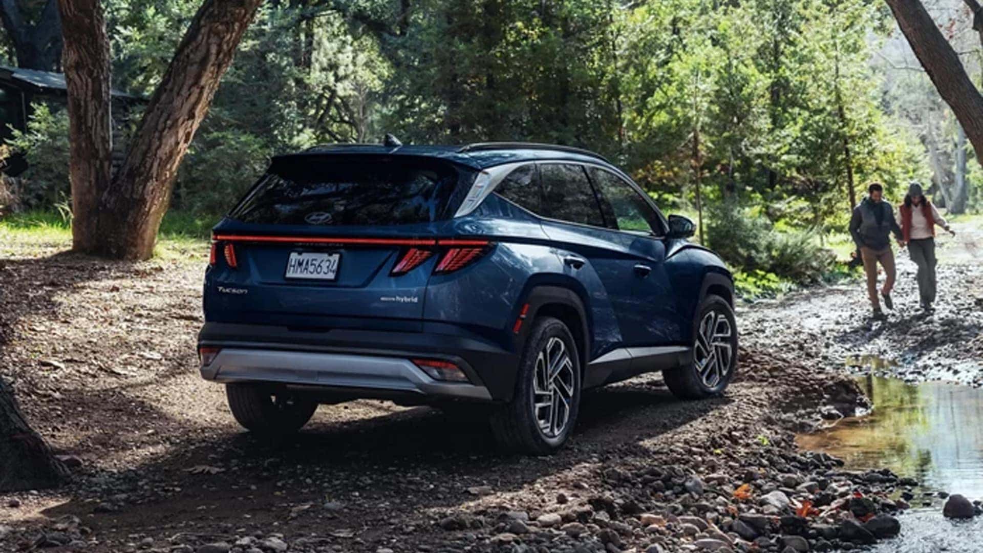 Blue Hyundai Tucson Hybrid parked on a forest trail with people walking nearby, illustrating versatility, trims, and outdoor lifestyle appeal.