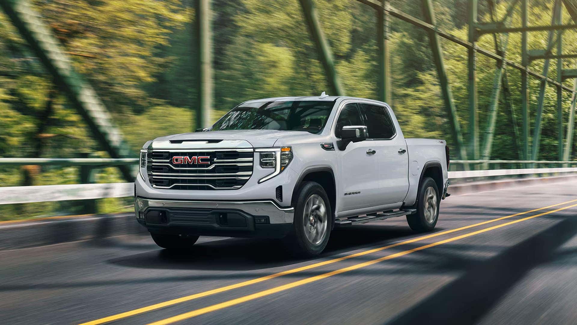 White 2026 GMC Sierra 1500 driving across a bridge, illustrating full-size truck proportions and exterior dimensions.