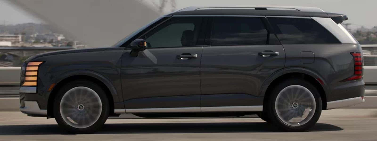 2026 Hyundai Palisade Hybrid driving on a city bridge, shown in side profile with aerodynamic SUV design and hybrid efficiency focus.