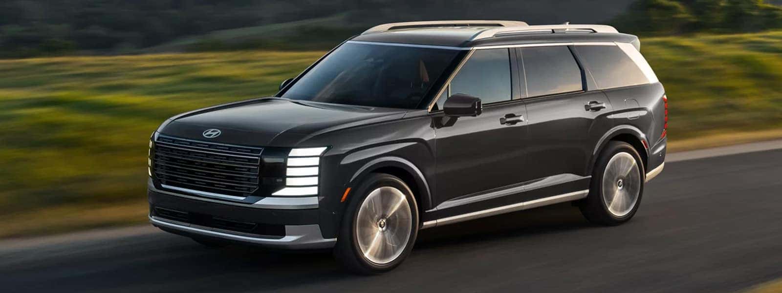 2026 Hyundai Palisade Hybrid driving on a scenic road, showing the front and side profile with modern grille and LED lighting