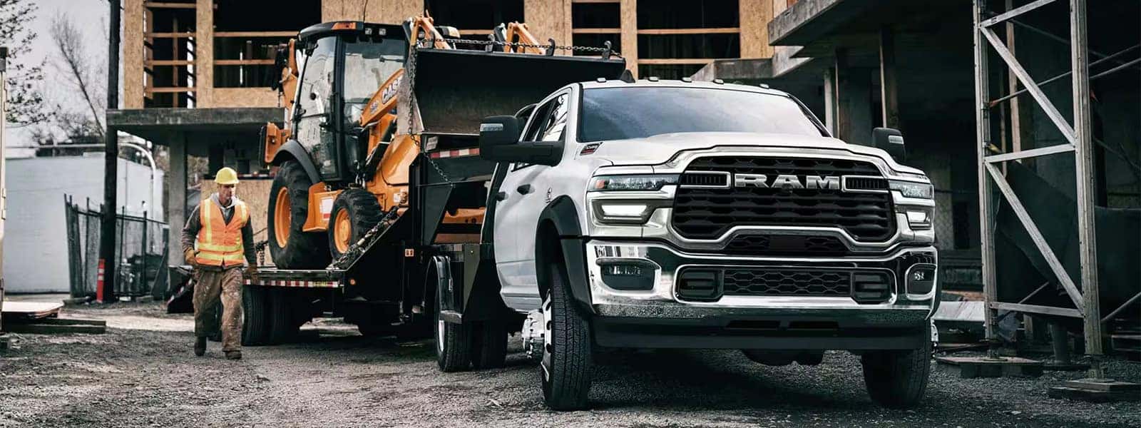 2026 Ram 1500 towing heavy construction equipment on a flatbed trailer at a job site