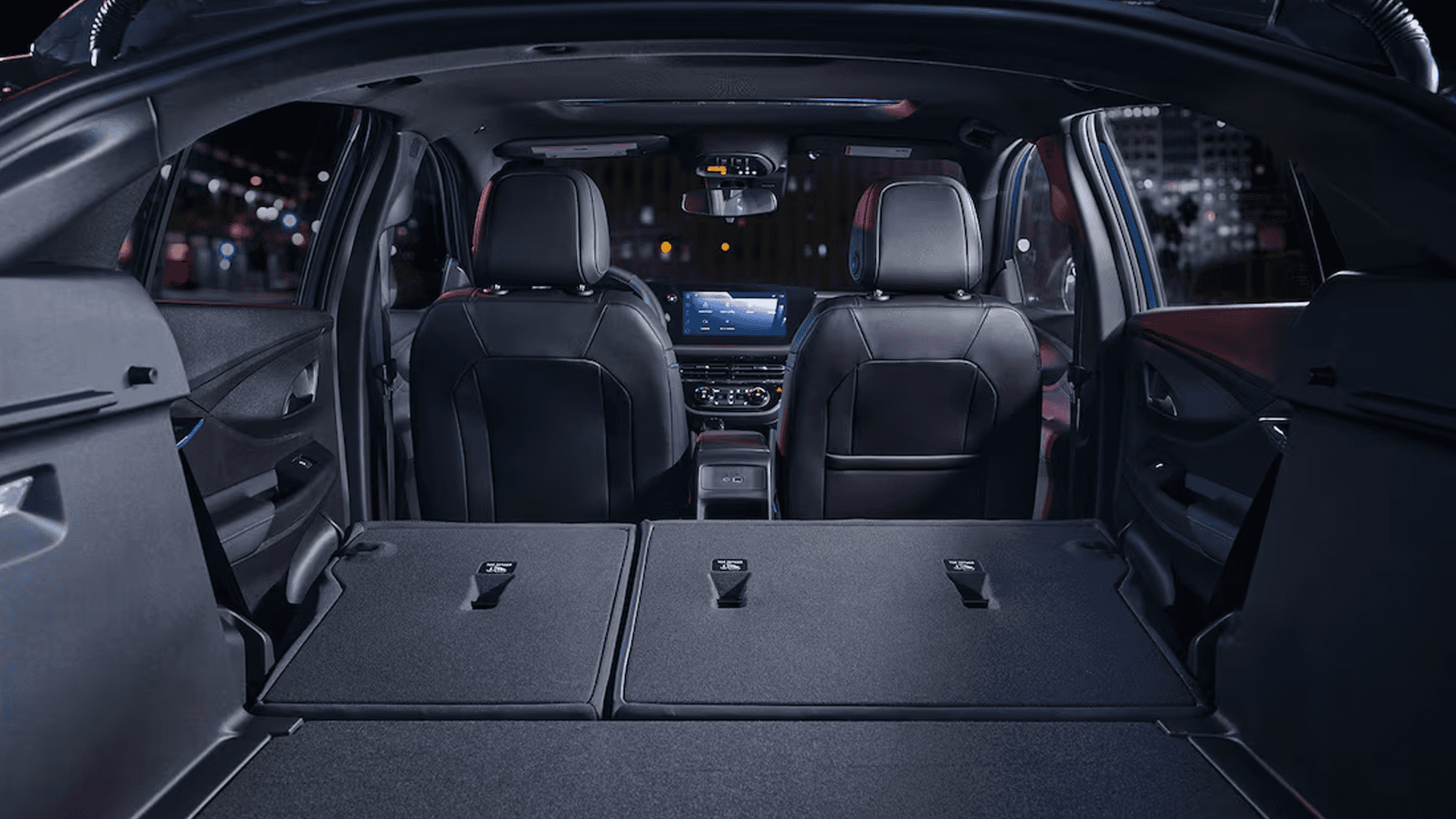 Rear cargo view inside the 2026 Buick Envista with the rear seats folded flat, showing a wide load floor, split seatback panels, and a clear line of sight to the front seats and center display at night