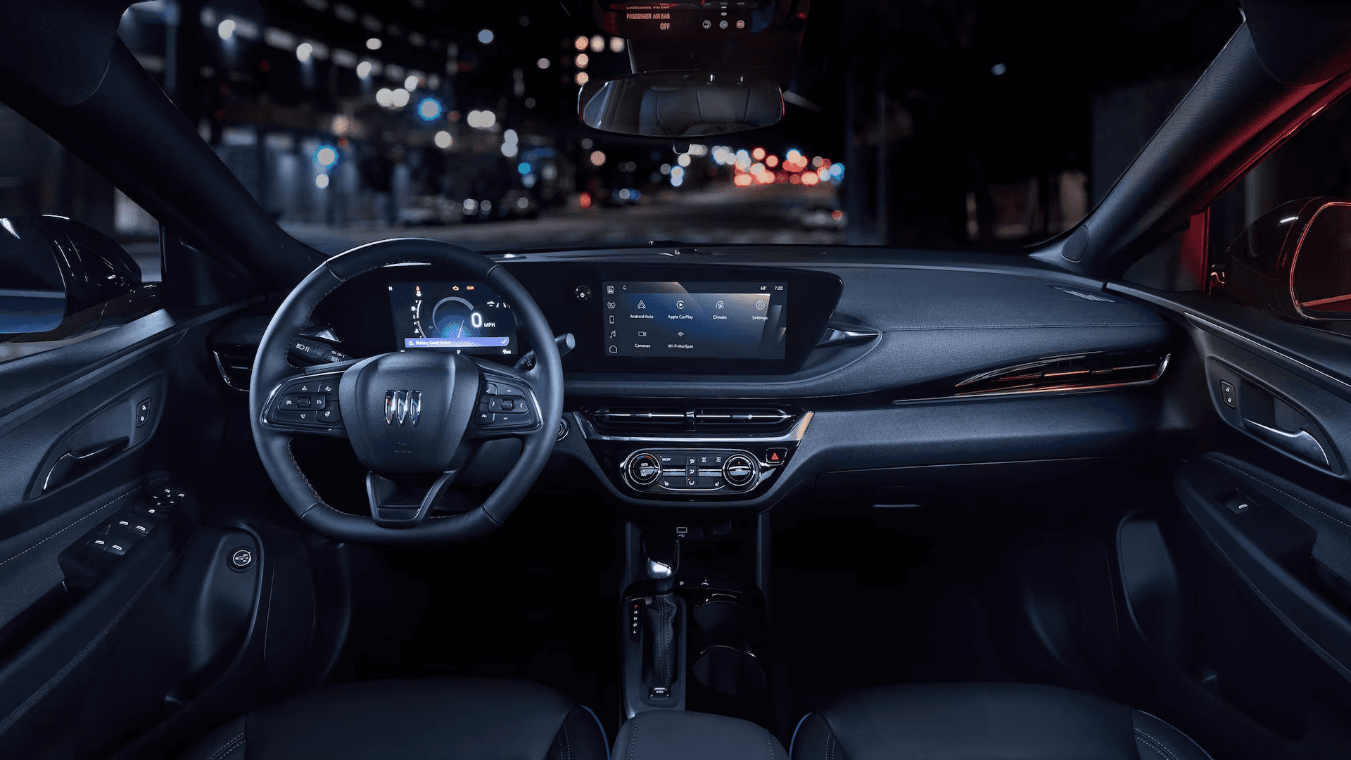 Wide interior view from the driver seat showing the steering wheel, digital gauge display, and center touchscreen, with night city lights visible through the windshield.