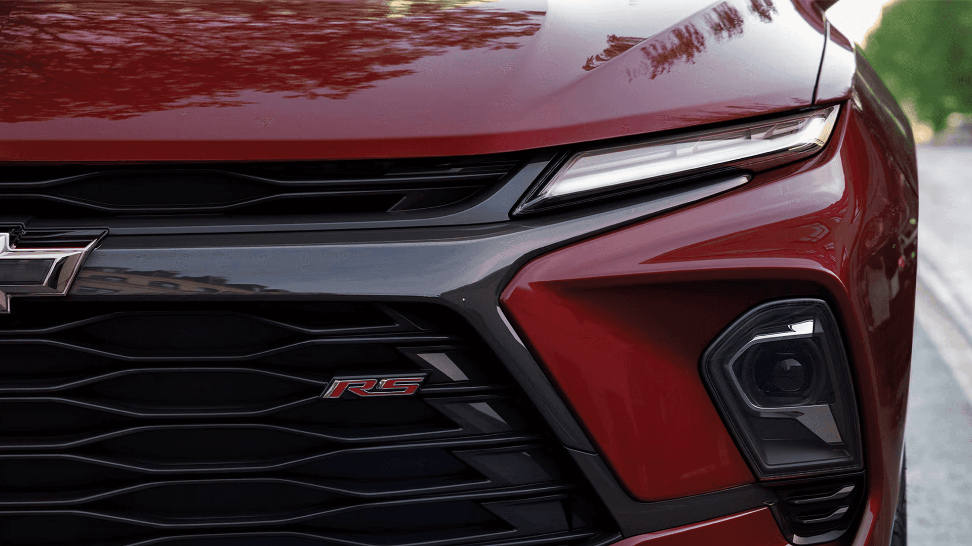 Close up of the front grille on a red 2026 Chevy Blazer RS, showing black grille elements, RS badge, and slim upper lighting.