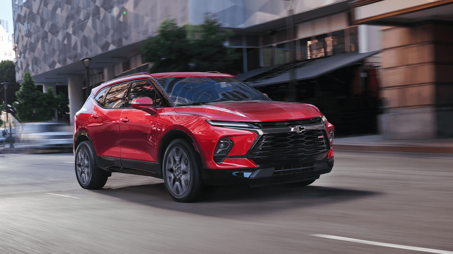 Red 2026 Chevy Blazer driving through a city street, shown from a front three quarter view with the grille, front fascia, and wheels visible.