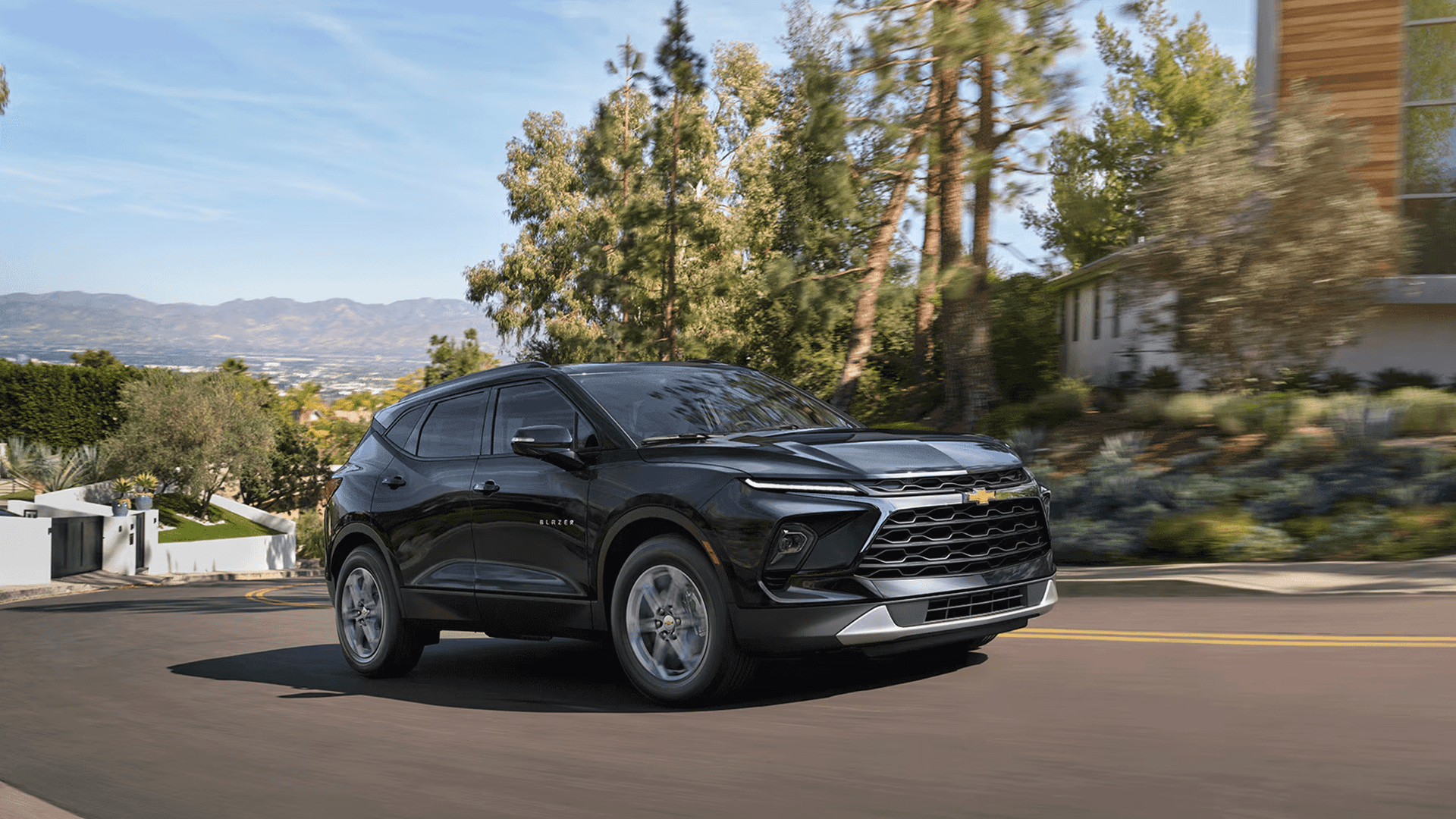Black 2026 Chevy Blazer driving on a winding road with trees and hills in the background