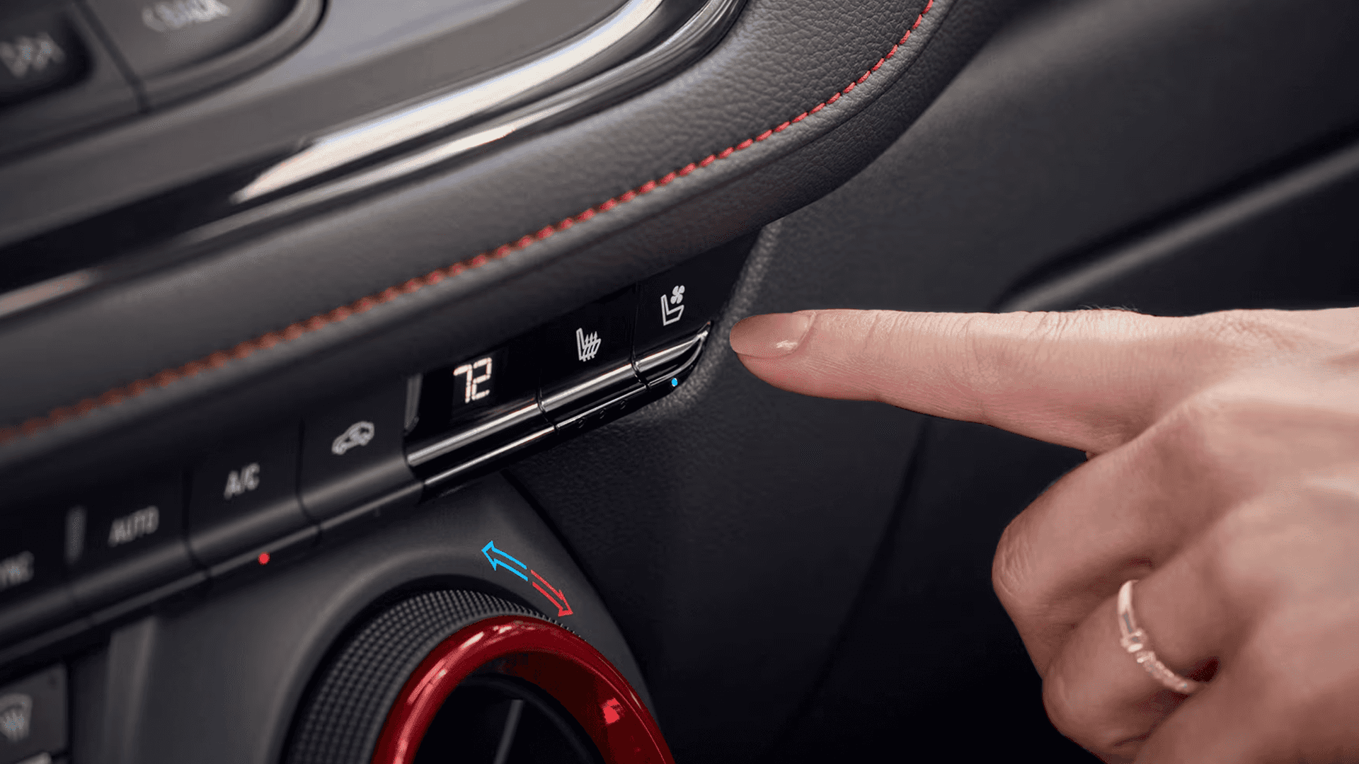 Wide front cabin view of the 2026 Chevy Blazer showing the steering wheel, gauge cluster, center touchscreen, circular air vents with red trim, gear shifter, dual cupholders, and black seats with red stitching.