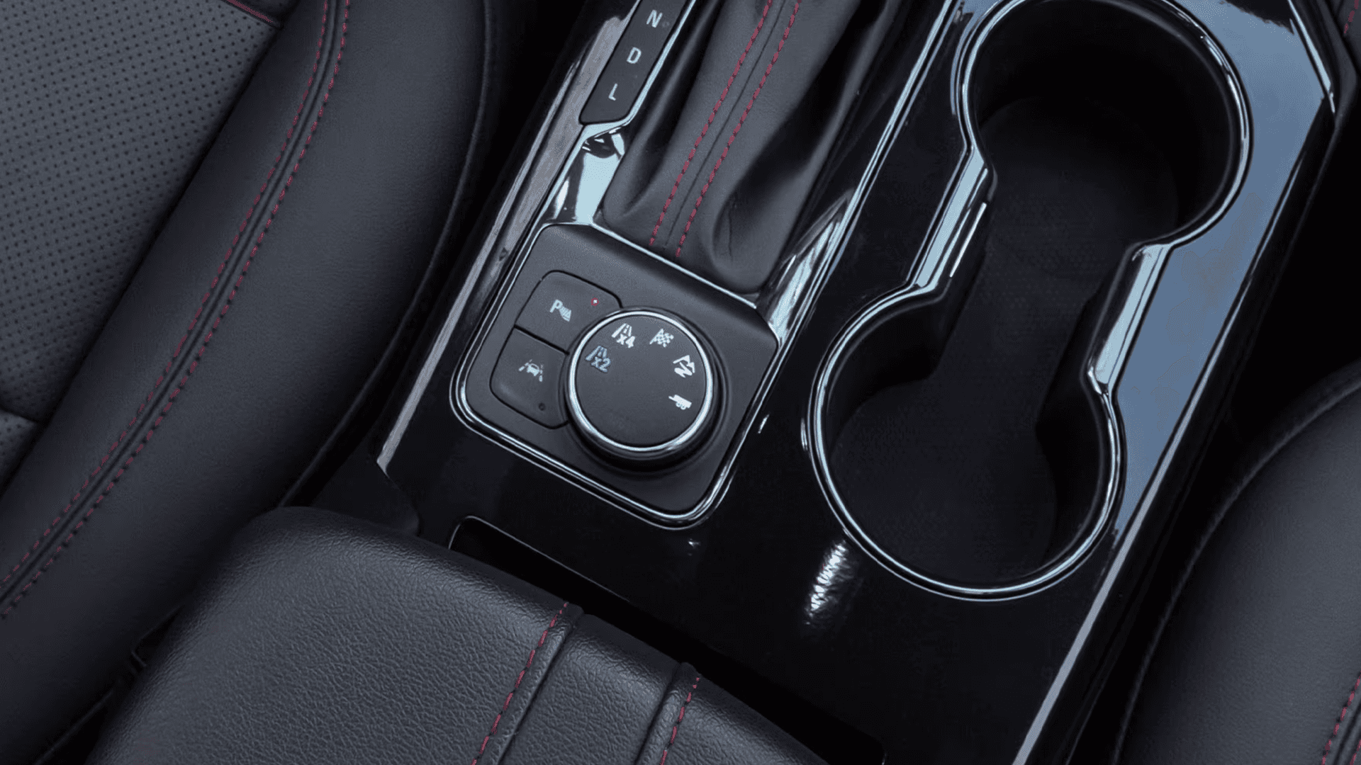 Close-up of the 2026 Chevy Blazer center console showing the drive mode selector knob with traction and drive settings, adjacent buttons, the gear selector, glossy black trim, and two cupholders.