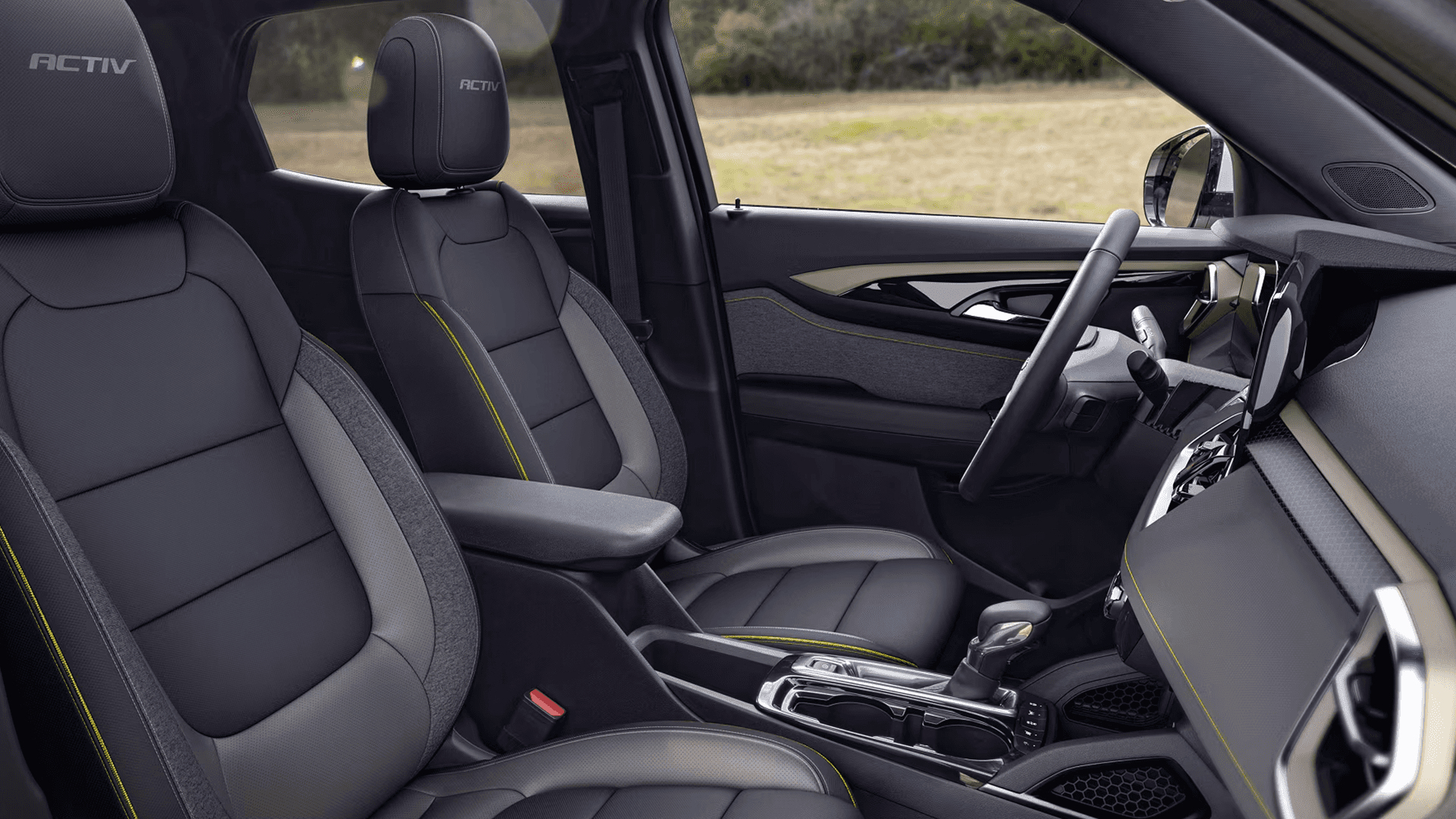 Interior view of a 2026 Chevrolet Trailblazer showing the front seats and dashboard from the passenger side, with ACTIV branding on the headrests, dark upholstery with contrast stitching, a center console with shifter and cupholders, and a wide infotainment screen angled toward the driver.