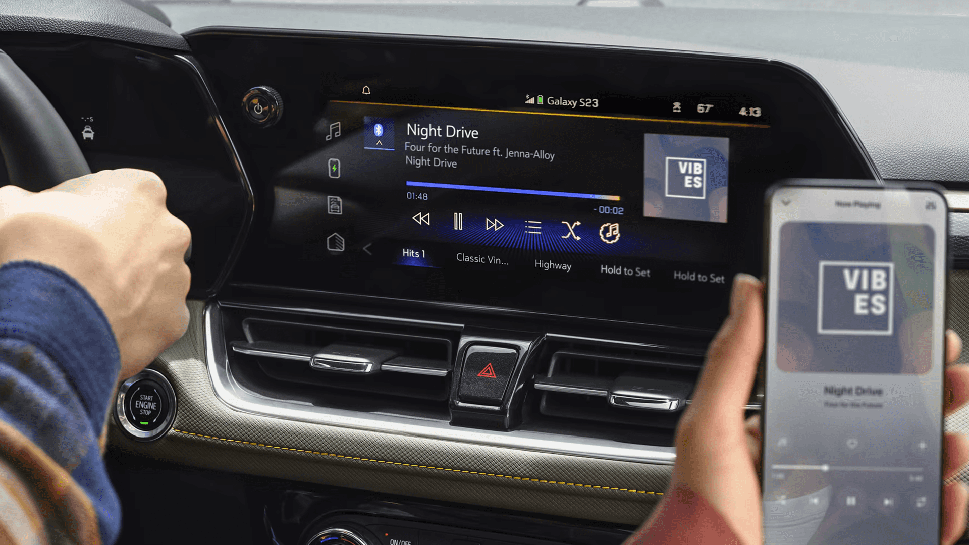 Infotainment touchscreen playing audio with smartphone connected, driver hand on wheel, and app interface shown.