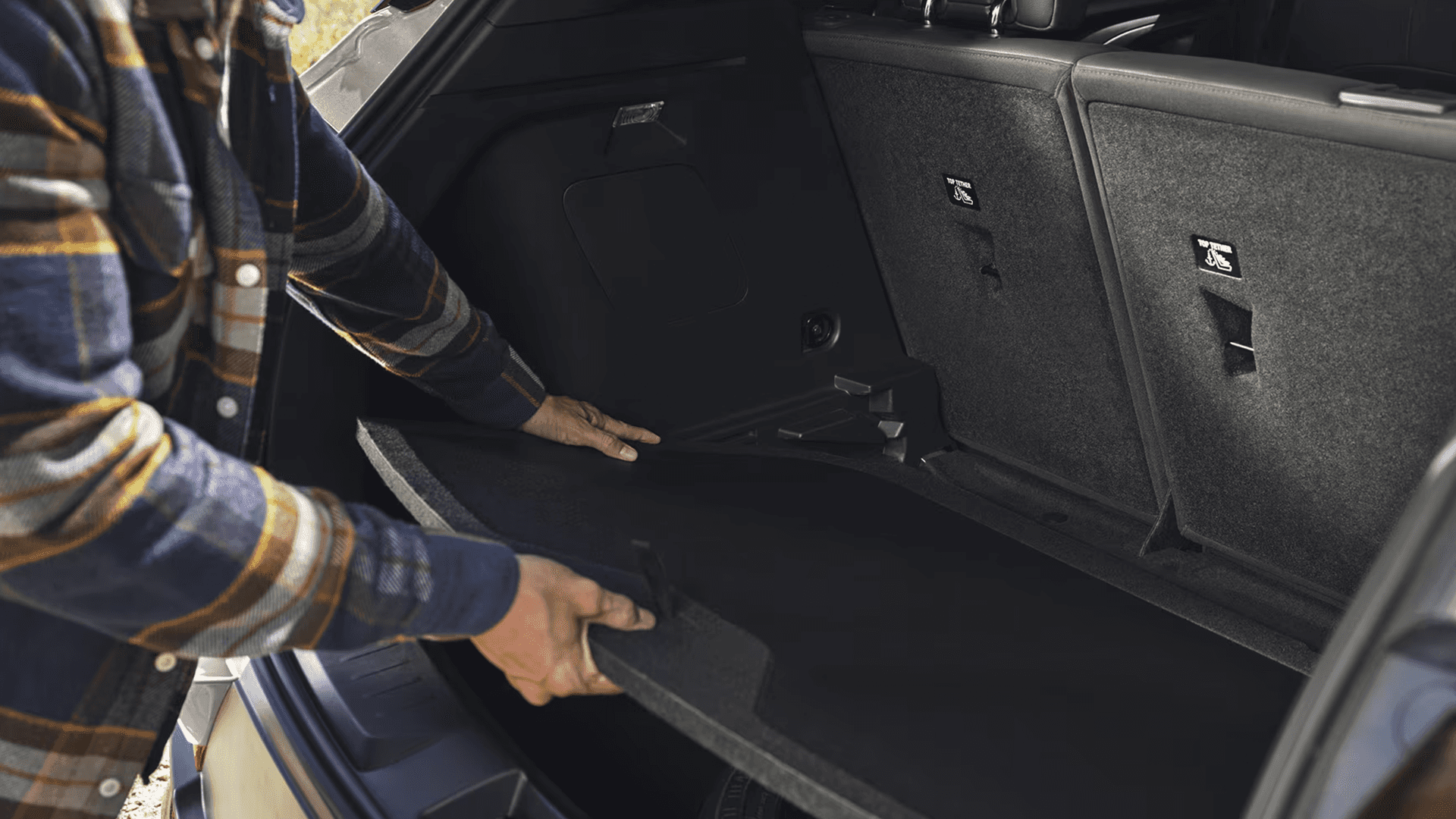 Rear cargo area with person lifting adjustable cargo floor panel in Trailblazer, seatbacks folded upright behind.
