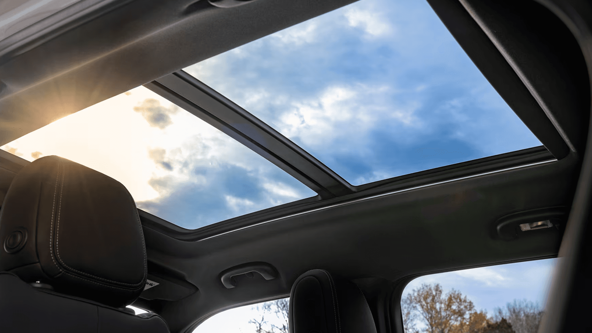 Upward view through panoramic sunroof showing blue sky and sun flare above the Trailblazer cabin.