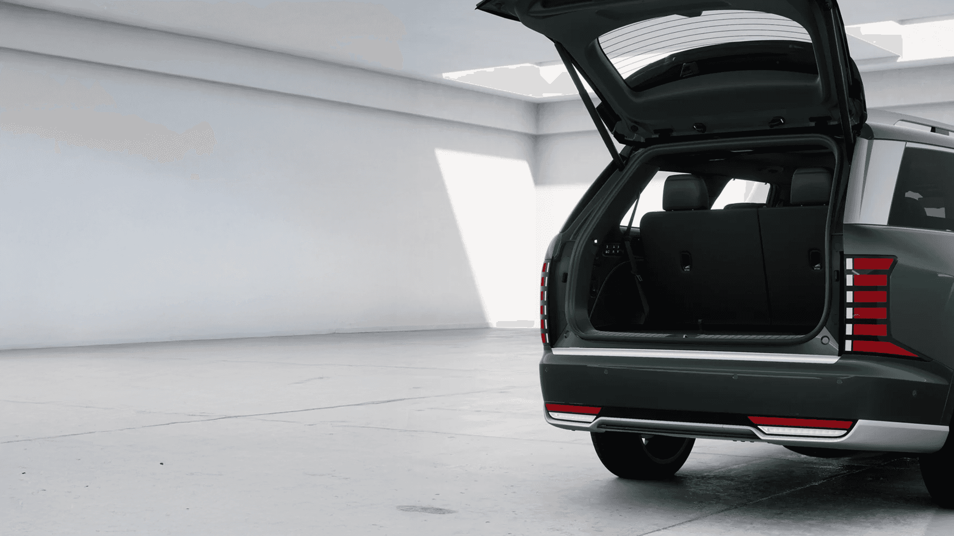 Rear corner view of a dark green 2026 Hyundai Palisade in a studio with the liftgate open, showing the large cargo opening, third-row seatbacks, vertical taillights, rear bumper, and lower silver trim.