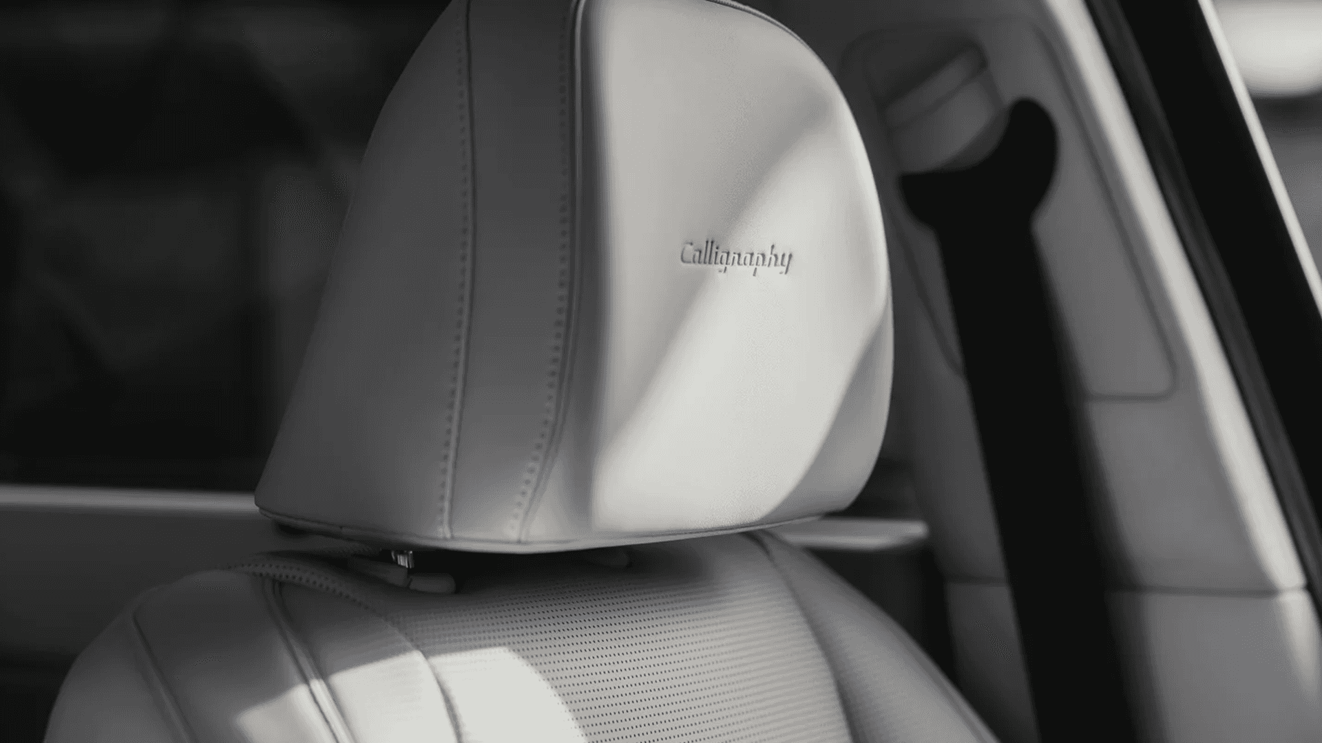 Close up of a light colored front seat headrest in a 2026 Hyundai Palisade with “Calligraphy” embossed, showing stitched leather, perforated seat surface, and a blurred view of the second row behind it.