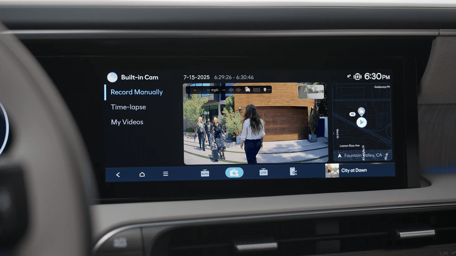 Wide infotainment screen showing a built in camera interface with options like Record Manually and Time lapse, a live video view of people near a garage, a map panel, and the time displayed at 6:30 PM.