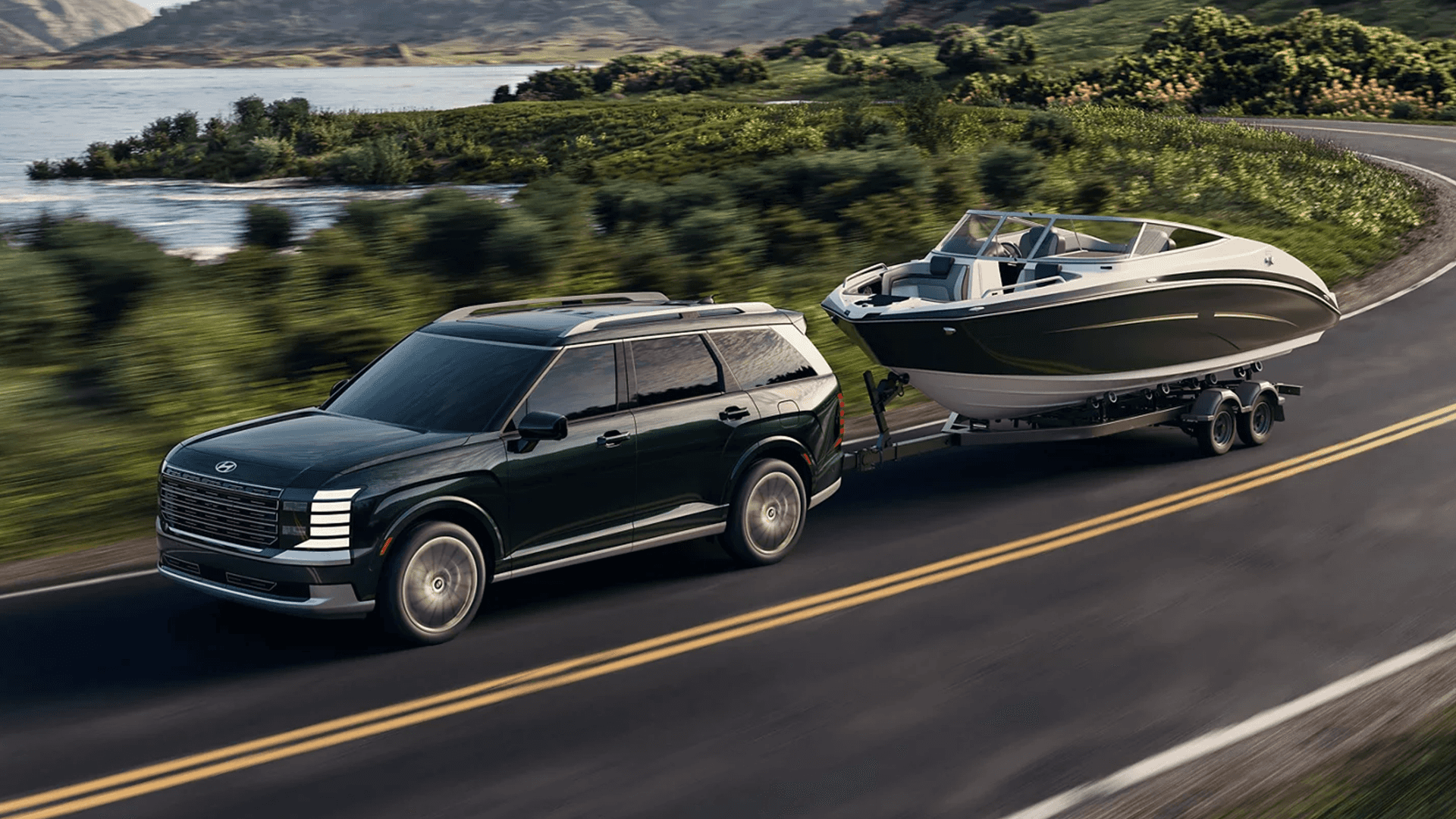 Dark green 2026 Hyundai Palisade towing a large black and white boat on a tandem axle trailer along a coastal highway, with ocean water to the left and green hills in the background.
